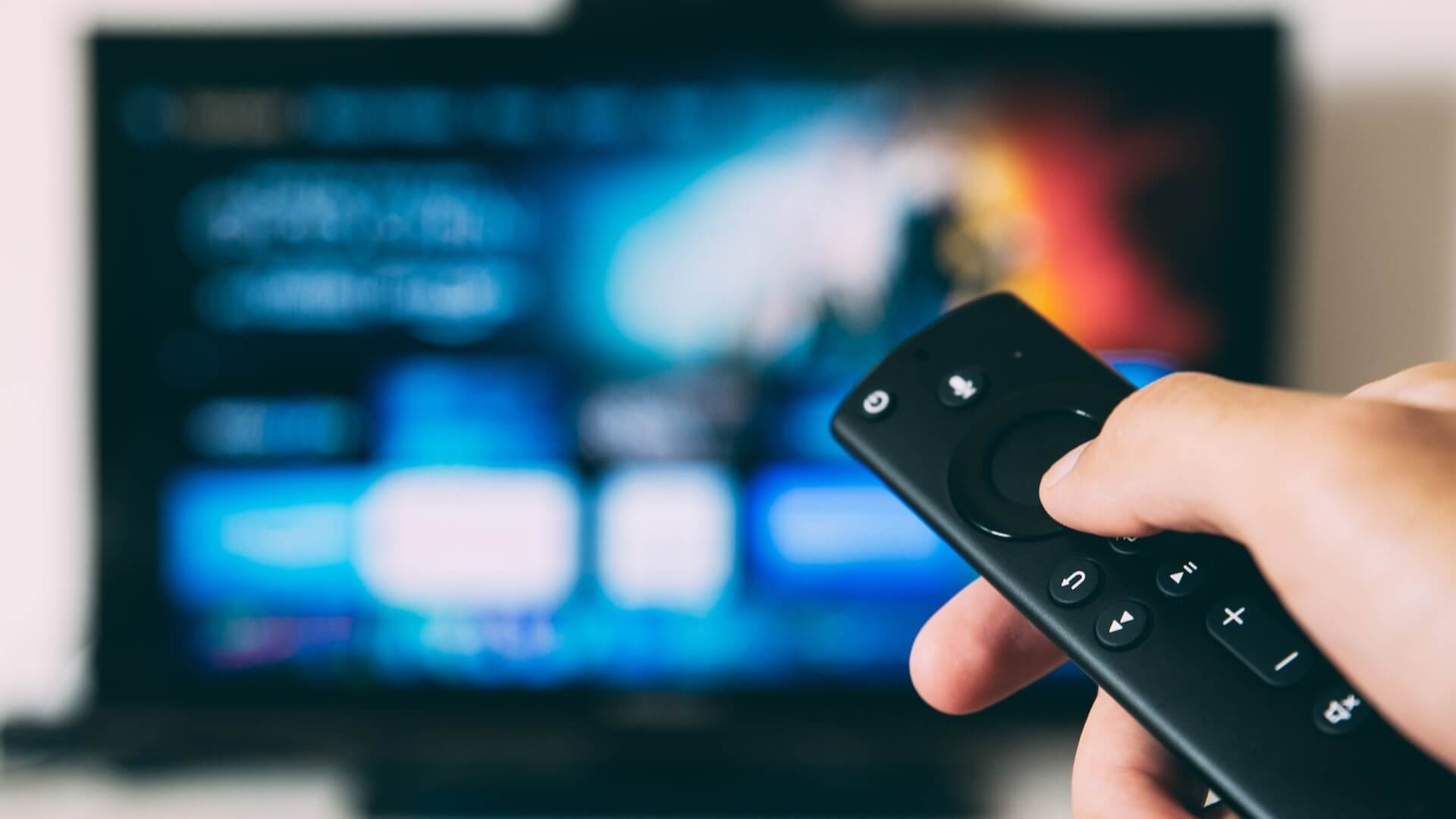 Person holding a remote in front of a blurred TV screen.