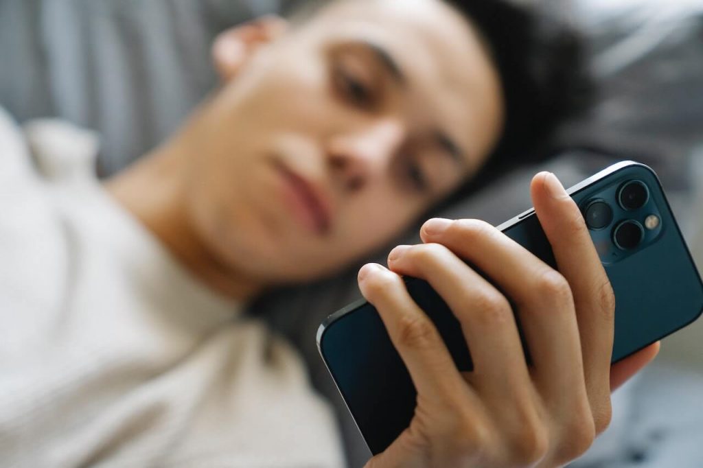 A man lying on a bed, using a sleep monitoring app on his phone